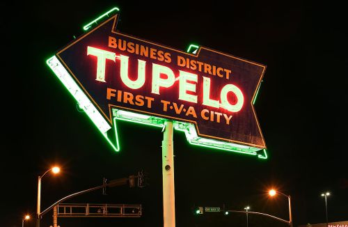 Neon sign for Tupelo, Mississippi, highlighting the business district and its title as the first TVA city, at night.