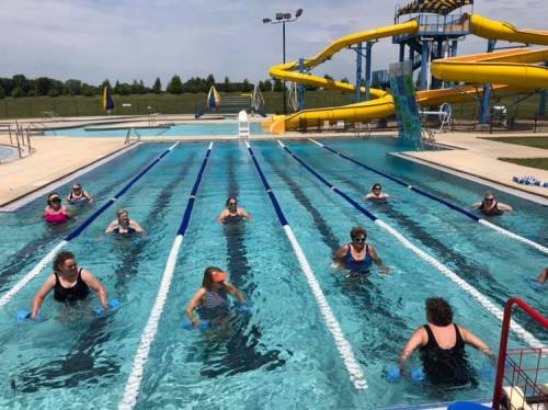 Aqua fitness class in a pool with participants exercising in the water, surrounded by slides and a sunny sky.