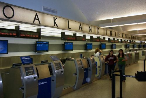 Interior of Oakland International Airport with check-in kiosks and travelers walking by.