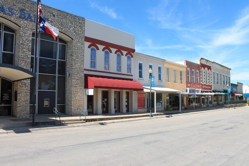 A quiet street scene featuring historic buildings with awnings, a Texas flag, and clear blue skies.