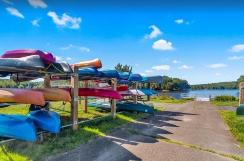 Colorful kayaks and canoes stacked on racks by a calm lake under a clear blue sky.