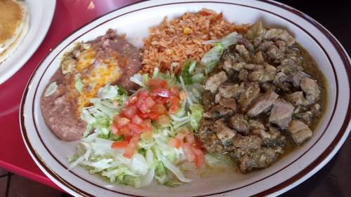 A plate of Mexican food featuring rice, refried beans, lettuce, tomatoes, and seasoned meat.