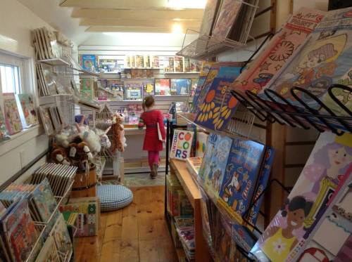 A child in a pink dress explores a colorful children's bookstore filled with books and toys.