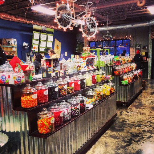 A colorful candy shop with jars of sweets on display, decorated with lights and a bicycle hanging from the ceiling.