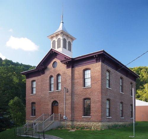 Historic brick building with a bell tower, surrounded by greenery and a clear blue sky.