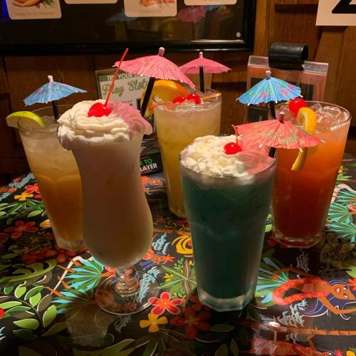 A colorful assortment of tropical cocktails with umbrellas and cherries, set against a vibrant floral tablecloth.
