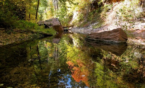 A serene creek surrounded by colorful autumn foliage and rocky banks, reflecting the vibrant trees in the water.
