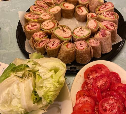 A platter of rolled sandwiches made with lettuce, turkey, and ham, alongside a plate of sliced tomatoes and a head of lettuce.