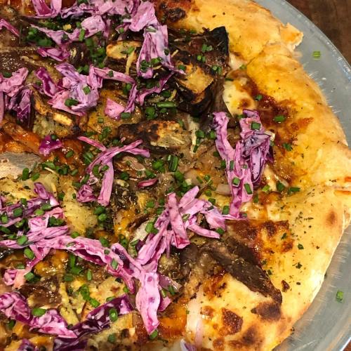 Close-up of a pizza topped with purple cabbage, chives, and various meats on a golden crust.