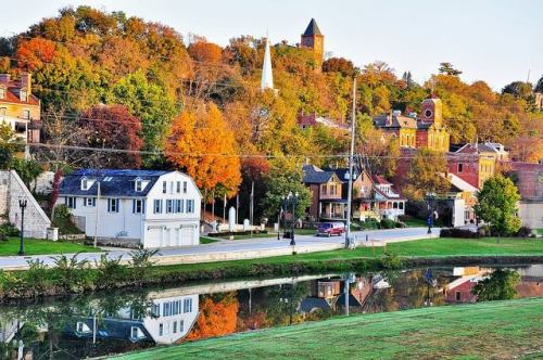 A picturesque town with colorful autumn trees, historic buildings, and a calm river reflecting the scenery.