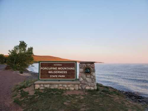 Sign for Porcupine Mountains Wilderness State Park by the water, with a scenic view of the mountains in the background.