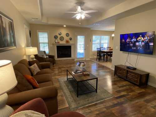 Cozy living room with a sofa, coffee table, and TV displaying a band, featuring a fireplace and dining area in the background.