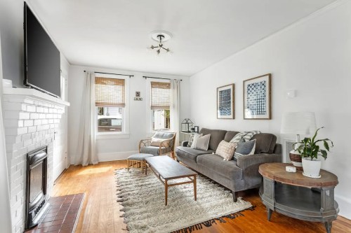 Cozy living room with a gray sofa, wooden coffee table, and a fireplace, featuring light curtains and decorative wall art.