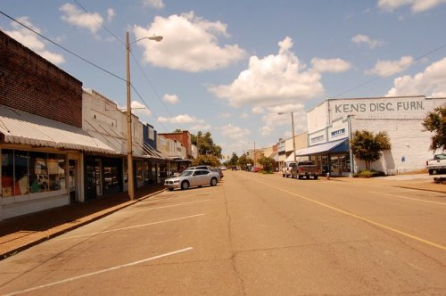 A quiet street lined with small shops and a blue sky with fluffy clouds overhead.