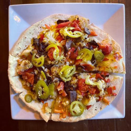 A flatbread topped with colorful vegetables, jalapeños, and seasoned meat, served on a square plate.
