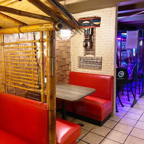 A cozy, tropical-themed seating area with bamboo decor and red booths in a dimly lit restaurant.