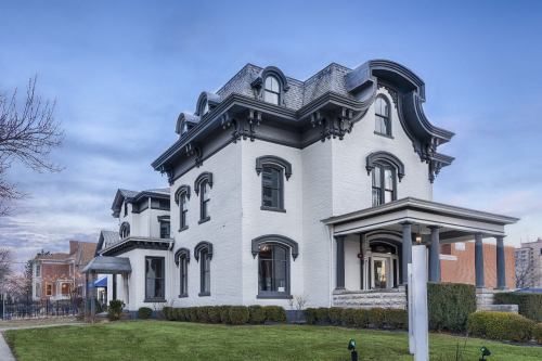 A large, historic gray house with ornate architectural details and a well-maintained lawn under a clear blue sky.