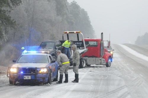 Emergency responders assist a vehicle on an icy road during a winter storm, with police and tow truck present.