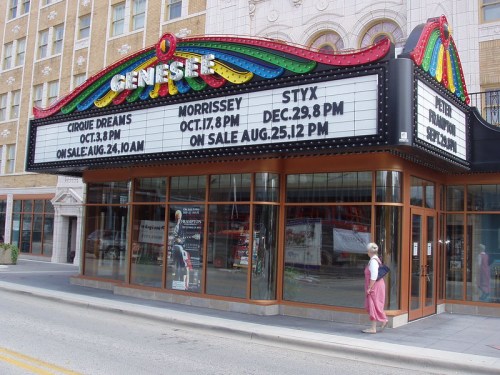 Marquee of the Genesee Theatre displaying upcoming events and showtimes, with a person walking by.
