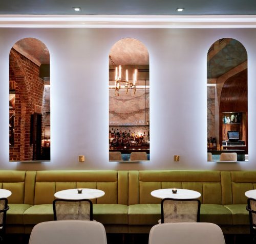 A stylish restaurant interior featuring green seating, round tables, and arched mirrors with soft lighting.