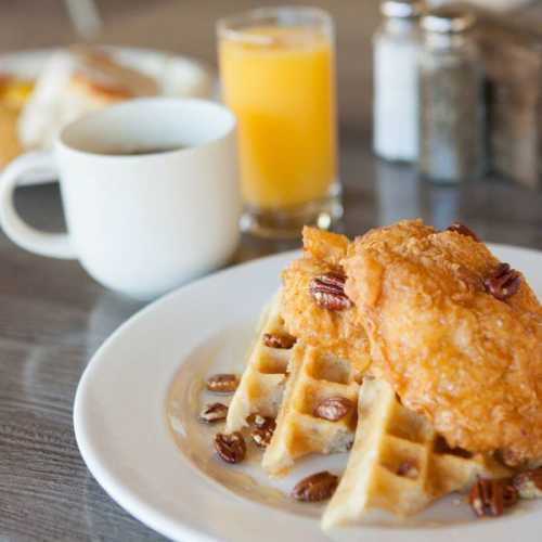 A plate of crispy fried chicken on waffles, garnished with pecans, with coffee and orange juice in the background.