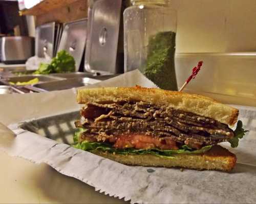 A stacked sandwich with layers of meat, lettuce, and tomato, served on toasted bread with a toothpick.