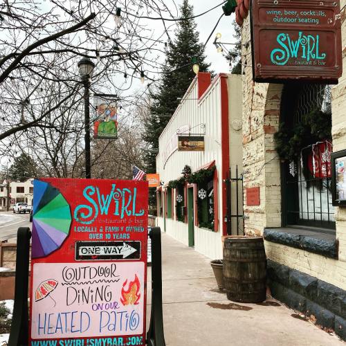 A colorful sign outside Swirl restaurant promotes outdoor dining on a heated patio, with festive decorations nearby.