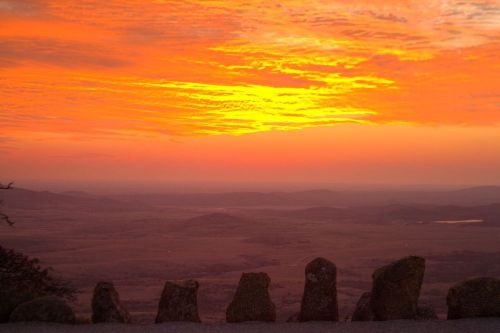 A vibrant orange sunset over rolling hills, with silhouetted rocks in the foreground.