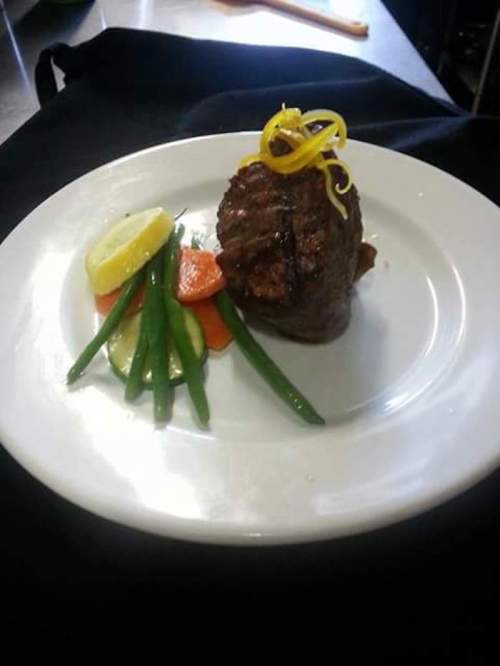 A plated dish featuring a grilled steak topped with lemon slices, accompanied by green beans and mixed vegetables.