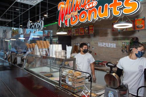 A vibrant dessert shop with staff serving ice cream and donuts, featuring colorful signage and a variety of toppings.