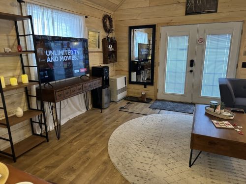 Cozy living room with a TV, wooden furniture, a rug, and large windows, creating a warm, inviting atmosphere.