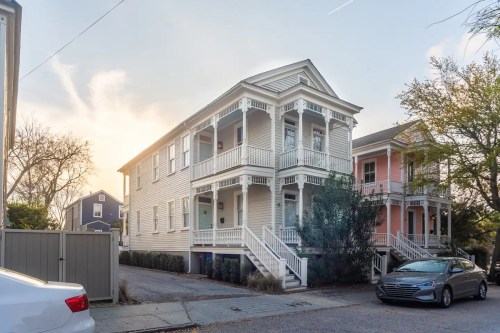 A two-story, light-colored house with porches, surrounded by trees and a driveway, under a clear sky at sunset.