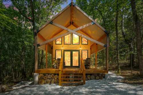 A modern cabin with large windows, surrounded by trees, featuring a wooden porch and rocking chairs.