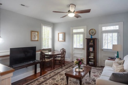 Cozy living room with a TV, dining table, and white sofa, featuring large windows and a decorative rug.