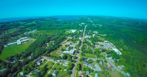 Aerial view of a lush green landscape with a small town, roads, and a lake in the distance under a clear blue sky.