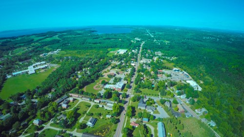 Aerial view of a green landscape with a small town, roads, and a lake in the distance under a clear blue sky.