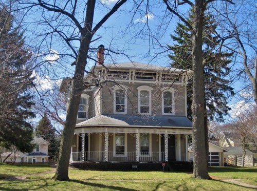 A large, two-story house with a porch, surrounded by trees and a clear blue sky.