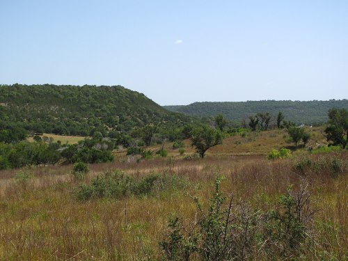 A scenic landscape featuring rolling hills, green vegetation, and a clear blue sky.