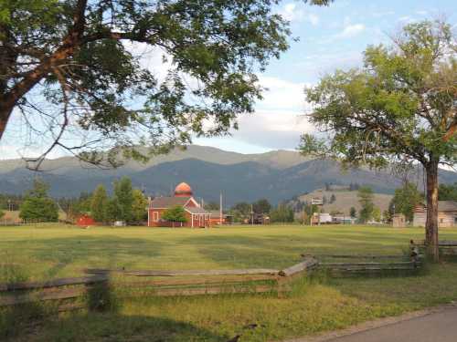 A scenic view of a red building surrounded by green fields, with mountains and trees in the background.