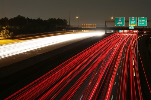 Long exposure shot of a highway at night, showing streaks of red and white lights from moving vehicles and road signs.
