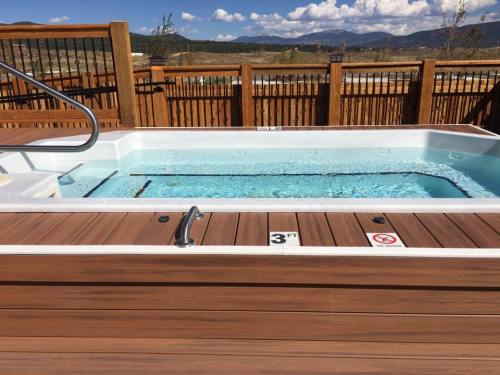 A hot tub with clear water, surrounded by wooden decking and a fence, set against a scenic mountain backdrop.