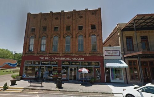 Historic brick buildings housing a grocery store and a bookstore, with outdoor seating and a clear blue sky.