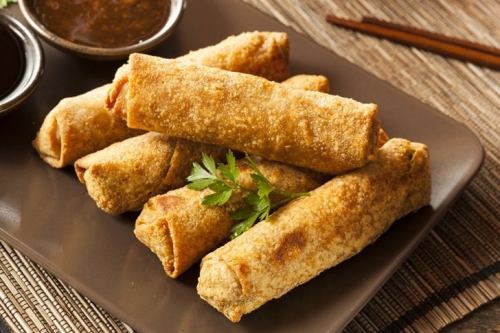 Crispy golden spring rolls served on a plate with dipping sauce and chopsticks in the background.