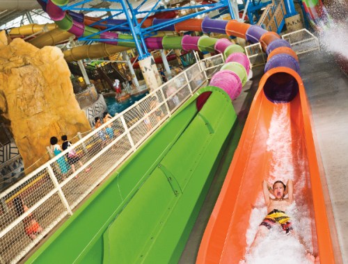 A child joyfully slides down a colorful water slide in a vibrant indoor water park.