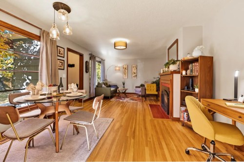 A cozy living and dining area with a round table, chairs, a fireplace, and a desk, featuring warm wood tones and natural light.