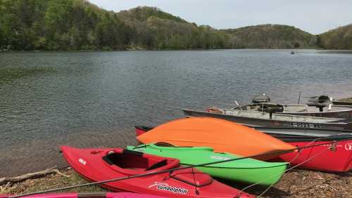 Colorful kayaks and a small boat are docked by a calm lake surrounded by lush green hills.