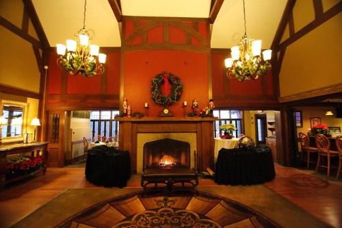 Cozy lodge interior with a fireplace, festive decorations, and elegant chandeliers, creating a warm atmosphere.