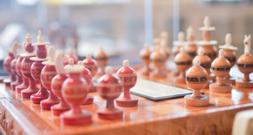 A close-up of a decorative chess set with uniquely shaped pieces on a wooden board.