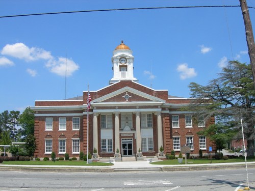 Historic brick building with a clock tower and golden dome, featuring columns and landscaped grounds under a blue sky.