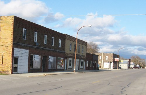 A quiet street lined with brick buildings under a partly cloudy sky.